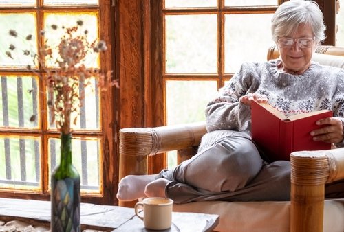 une senior en train de lire sur son fauteuil dans son chalet en bois habitat idéal pour senior